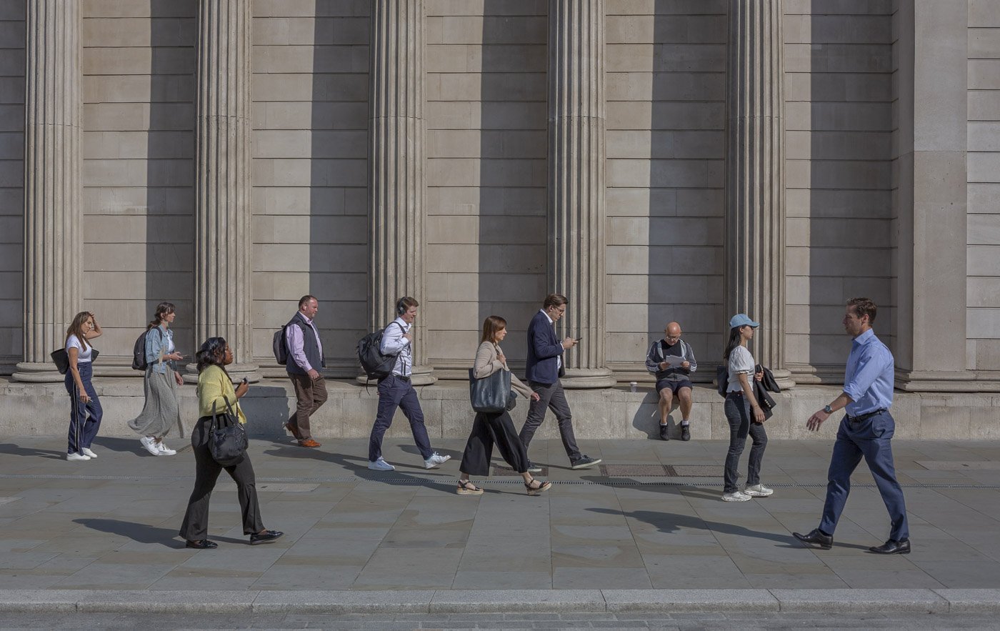 Commuters walking past a seated man outside Bank in London – photograph by Antony Zacharias.
